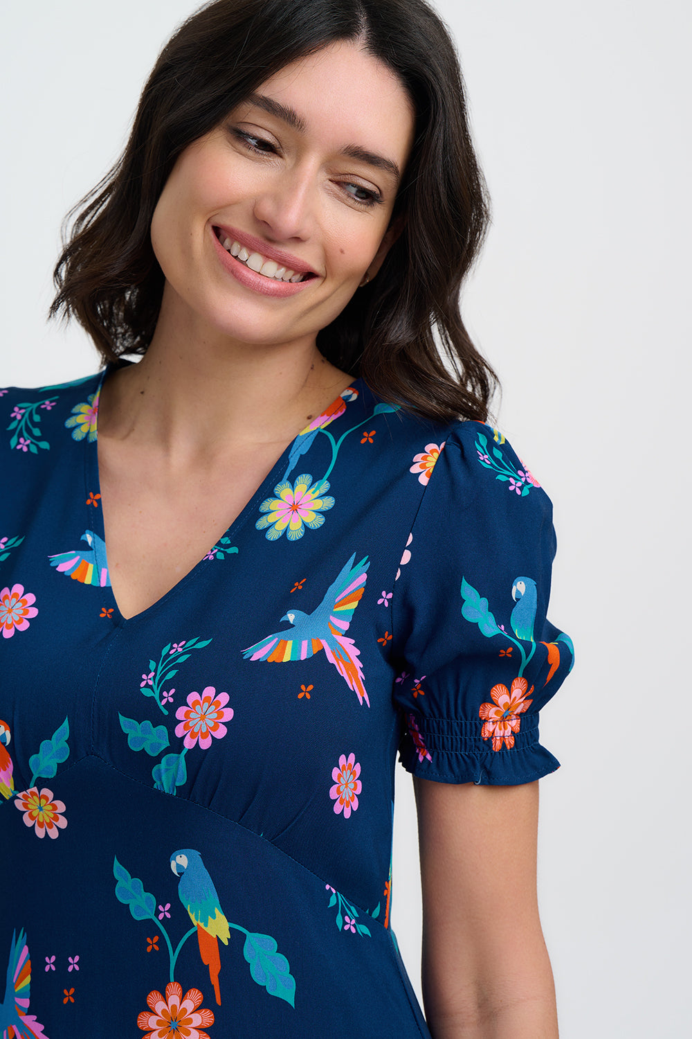 Woman wearing a navy blue dress with colorful parrot and flower pattern on a white background