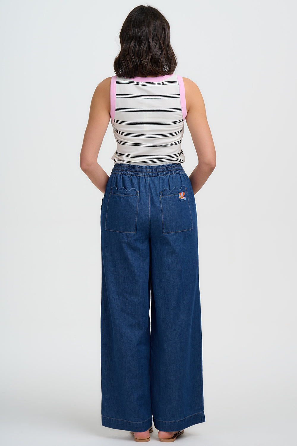 Person wearing a striped tank top and blue wide-leg pants on a white background
