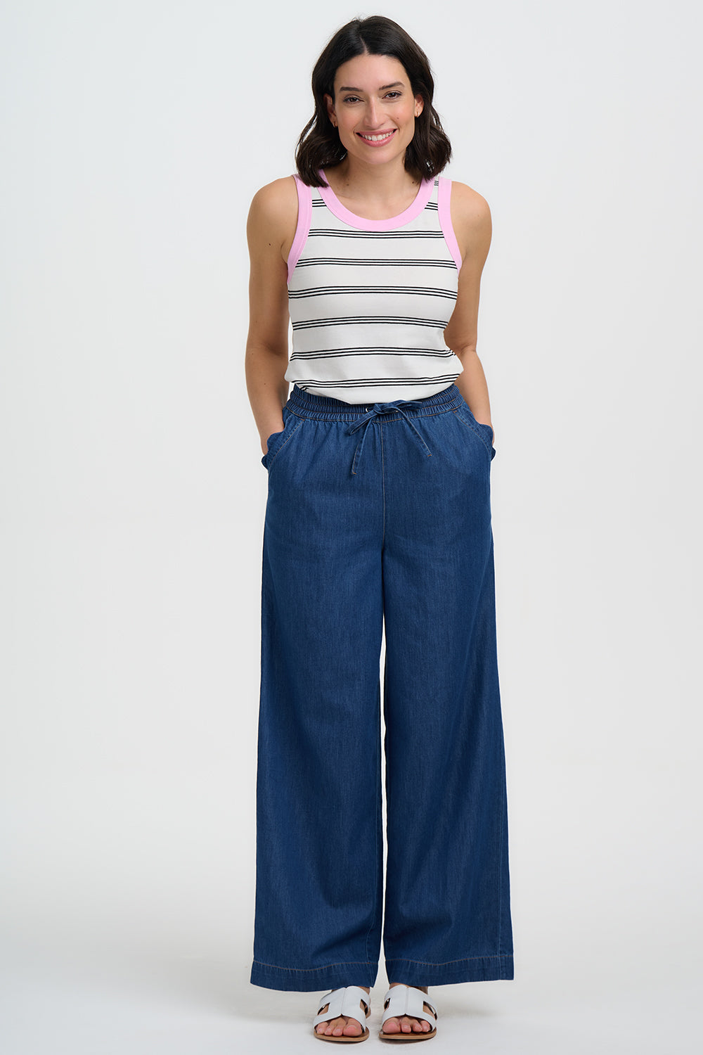 Woman wearing a striped tank top and blue wide-leg pants on a white background