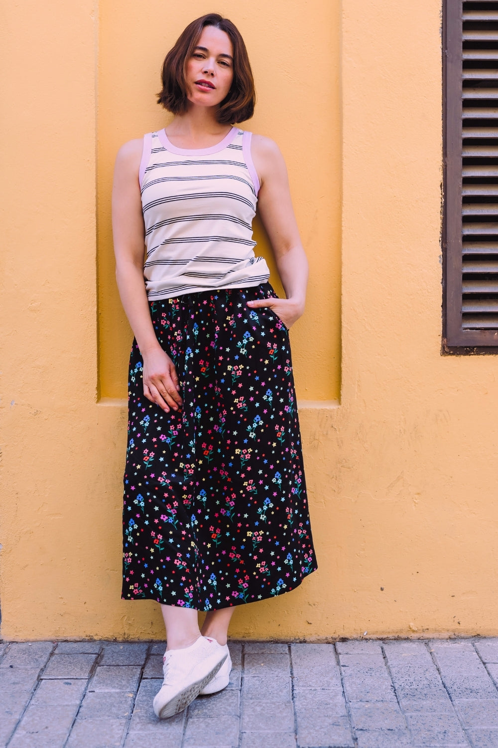 Woman wearing a striped tank top and colorful skirt against a yellow wall.