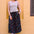 Woman wearing a striped tank top and colorful skirt against a yellow wall.