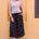 Woman wearing a striped tank top and colorful skirt against a yellow wall.