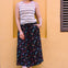 Woman wearing a striped tank top and colorful skirt against a yellow wall.