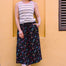 Woman wearing a striped tank top and colorful skirt against a yellow wall.