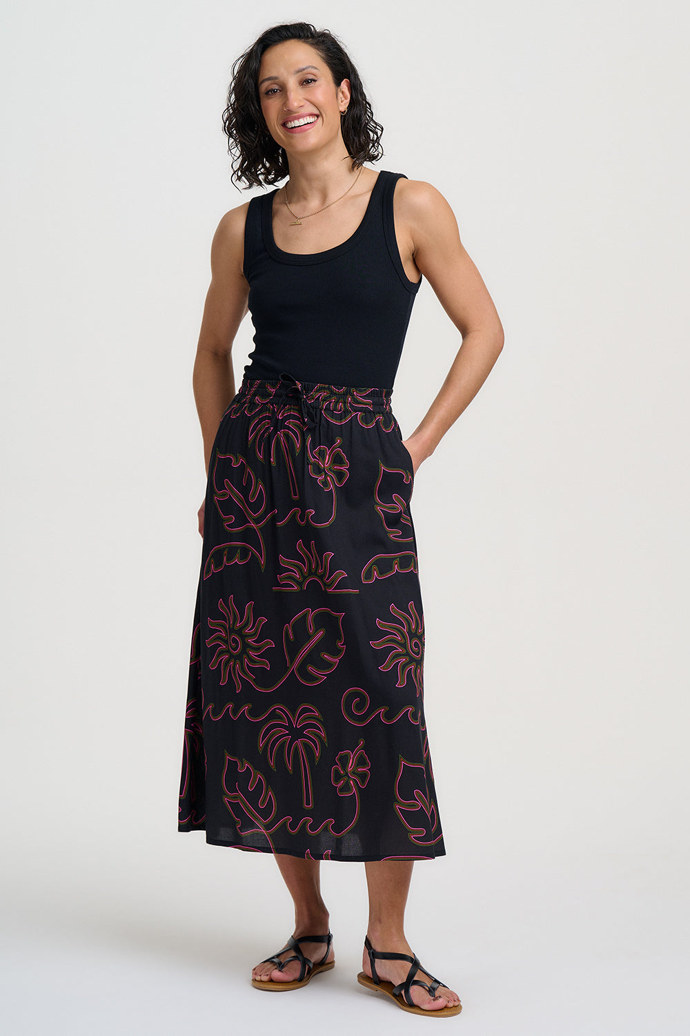 Woman wearing a black tank top and patterned black skirt on a white background