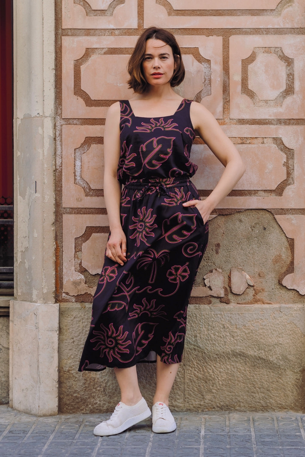 Woman wearing a dark floral dress standing against a textured wall.