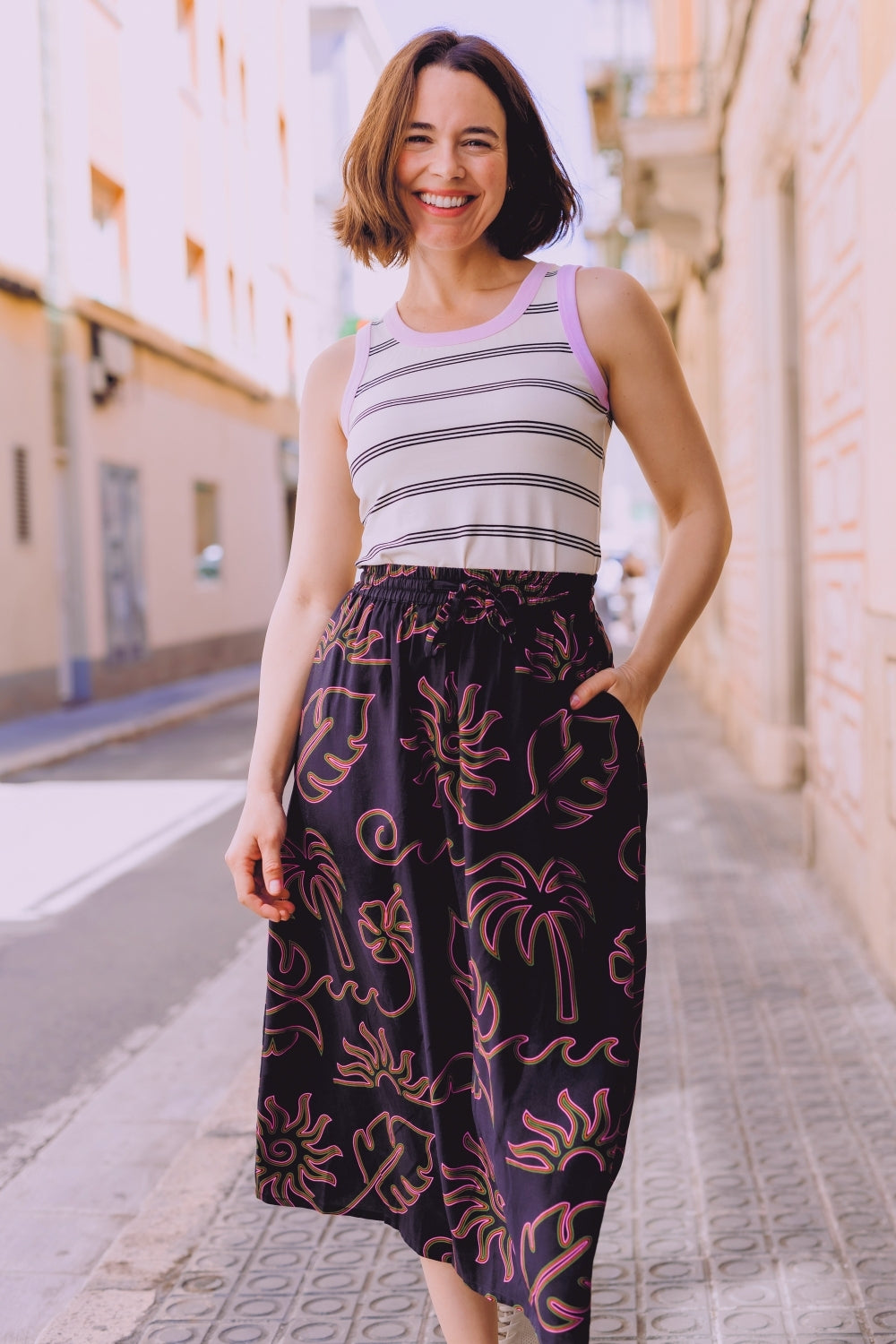 Woman wearing a striped tank top and patterned skirt standing on a street.
