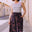 Woman wearing a striped tank top and patterned skirt standing on a street.