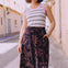Woman wearing a striped tank top and patterned skirt standing on a street.