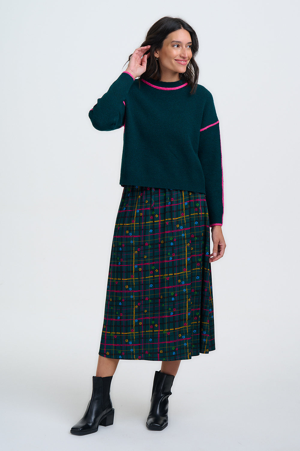 Woman wearing a dark green sweater with pink trim and a plaid skirt on a white background
