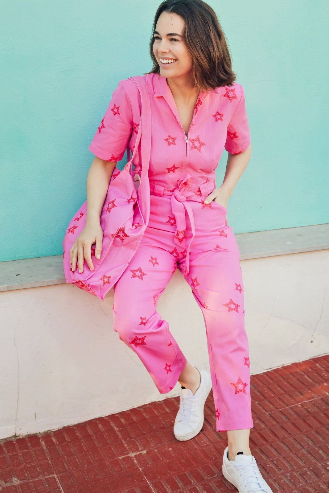 A person wearing a vibrant pink boilersuit with deep pink star shapes, featuring an open shirt collar, short sleeves, and a self-fabric belt.