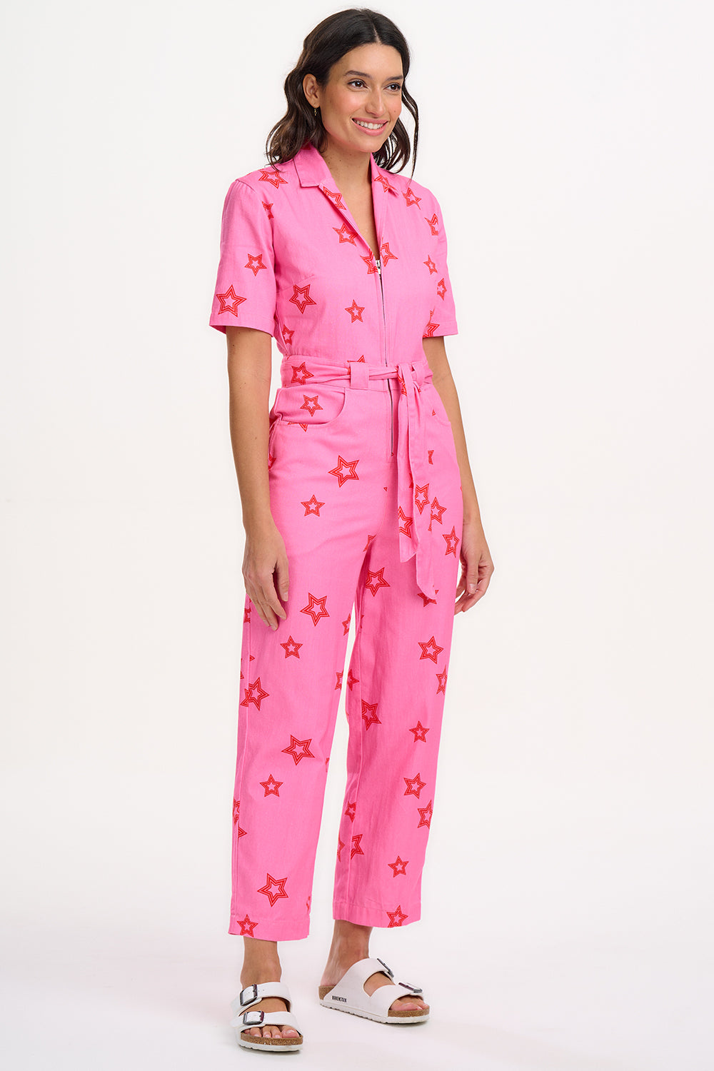 A woman modeling a short-sleeved pink boilersuit with a floral star pattern and a collar.