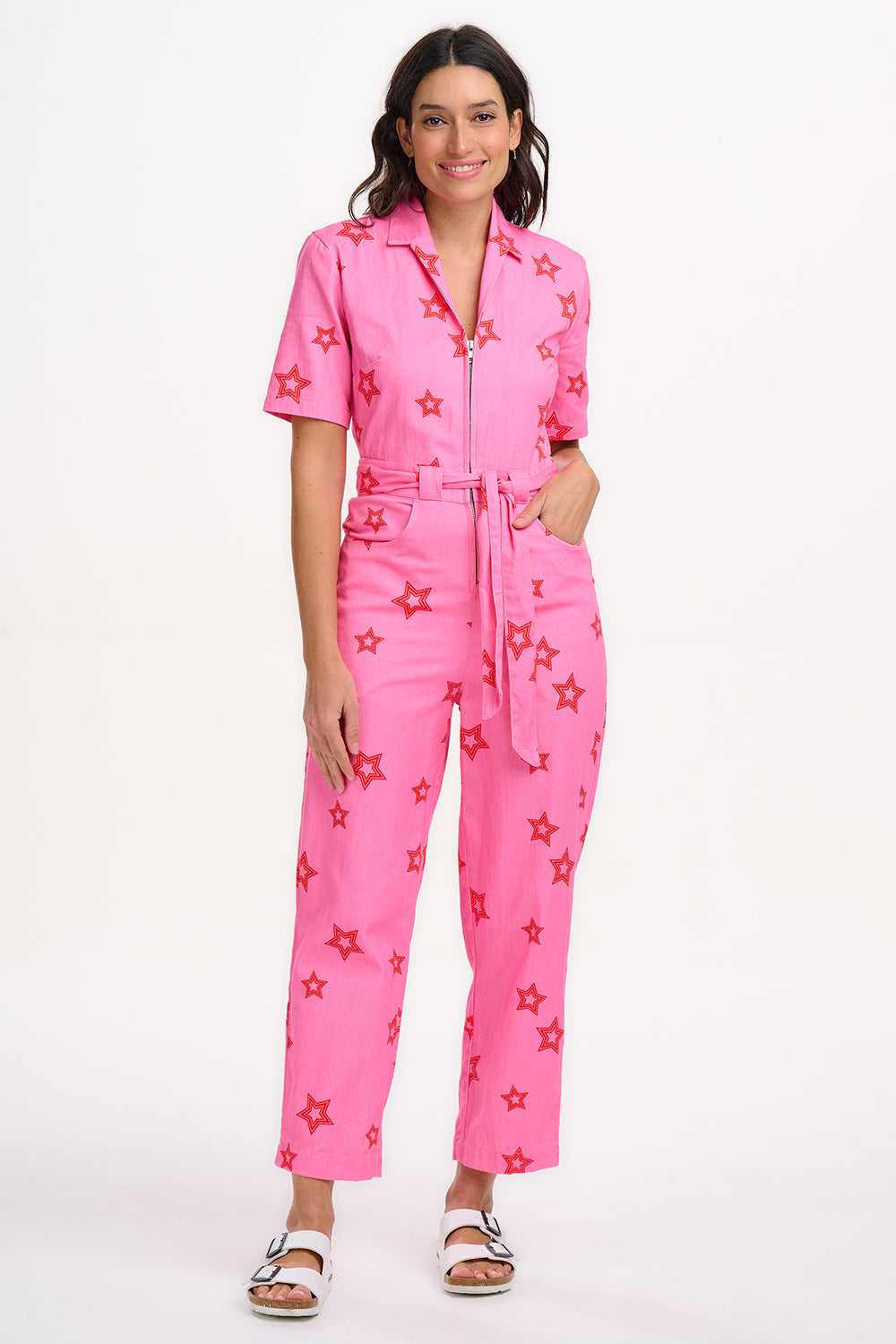 A woman modeling a short-sleeved pink boilersuit with a floral star pattern and a collar.