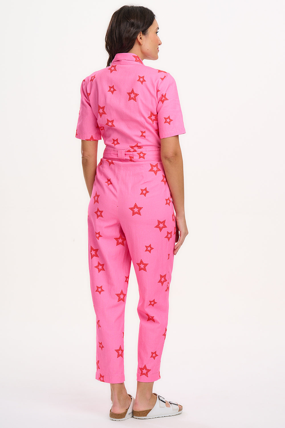A woman modeling a short-sleeved pink boilersuit with a floral star pattern and a collar.