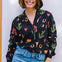 A woman wearing a black long-sleeved shirt with a cowgirl print of cactus, hearts, cowboy boots, and horseshoes, paired with blue jeans.