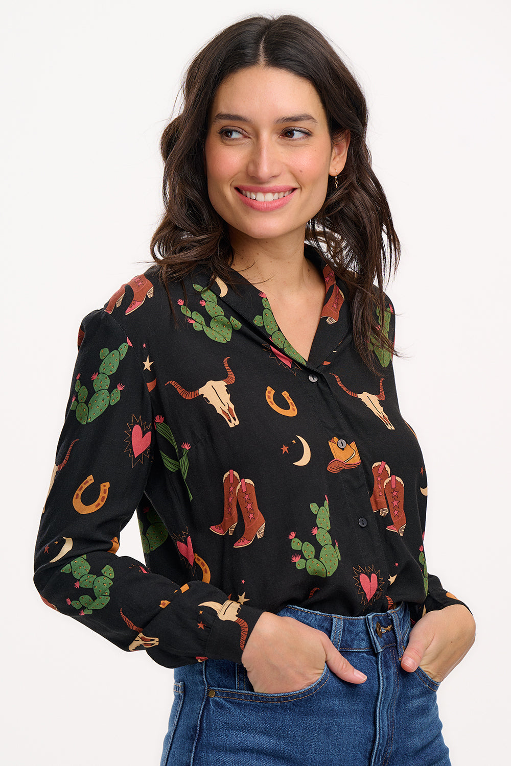 A woman wearing a black long-sleeved shirt with a cowgirl print of cactus, hearts, cowboy boots, and horseshoes, paired with blue jeans.