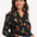 A woman wearing a black long-sleeved shirt with a cowgirl print of cactus, hearts, cowboy boots, and horseshoes, paired with blue jeans.