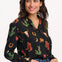 A woman wearing a black long-sleeved shirt with a cowgirl print of cactus, hearts, cowboy boots, and horseshoes, paired with blue jeans.