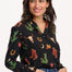 A woman wearing a black long-sleeved shirt with a cowgirl print of cactus, hearts, cowboy boots, and horseshoes, paired with blue jeans.