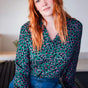 Woman with red hair wearing a patterned blouse sitting on a bench.