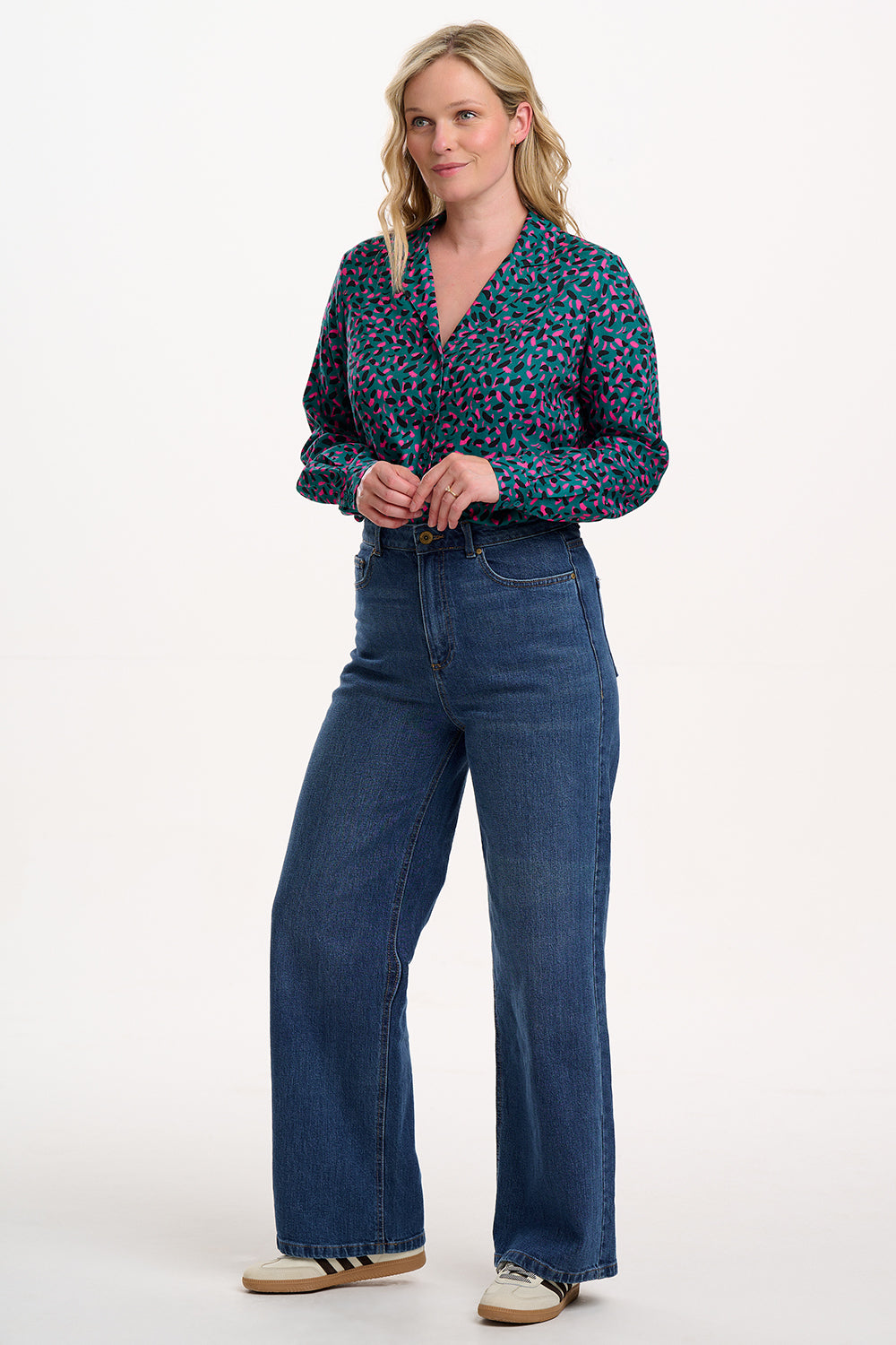 Woman wearing a patterned blouse and blue jeans on a white background