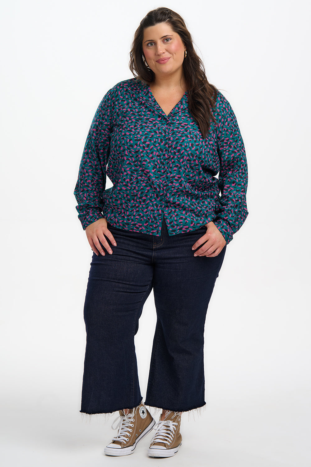 Woman wearing a patterned blouse and dark jeans on a white background