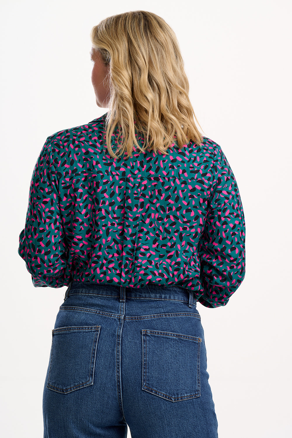 Person wearing a patterned blouse and blue jeans on a white background