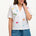 A model wearing an off-white shirt with a colorful fruit and cocktail themed pattern, paired with blue denim shorts.