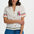 Woman wearing a white embroidered shirt with colorful accents and blue shorts on a white background