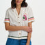 Woman wearing a white embroidered shirt with colorful accents and blue shorts on a white background