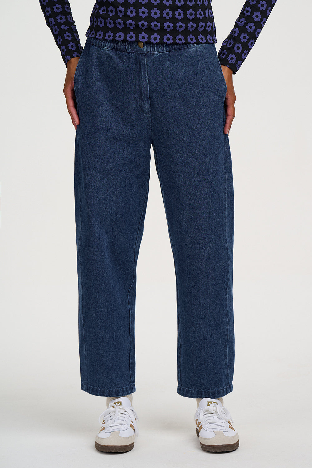 A person wearing dark blue wide-leg denim jeans, a patterned navy top, and white sneakers, shown from the waist down against a plain light background.