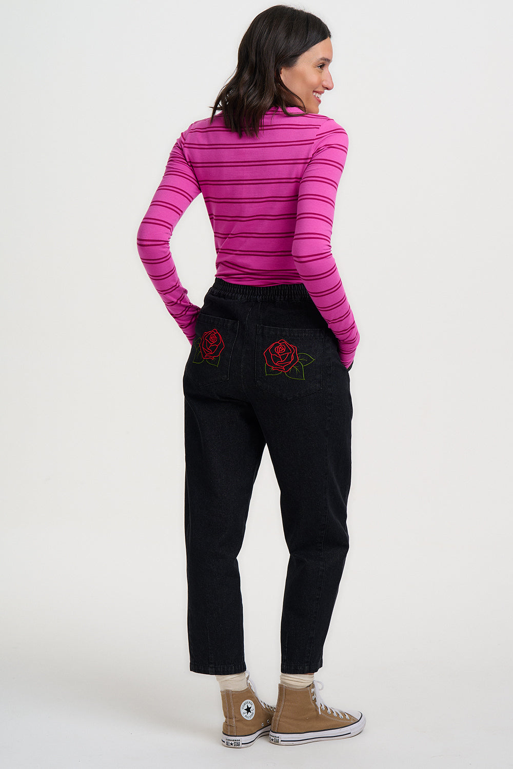 Person wearing a pink striped shirt and black pants with rose embroidery on a white background