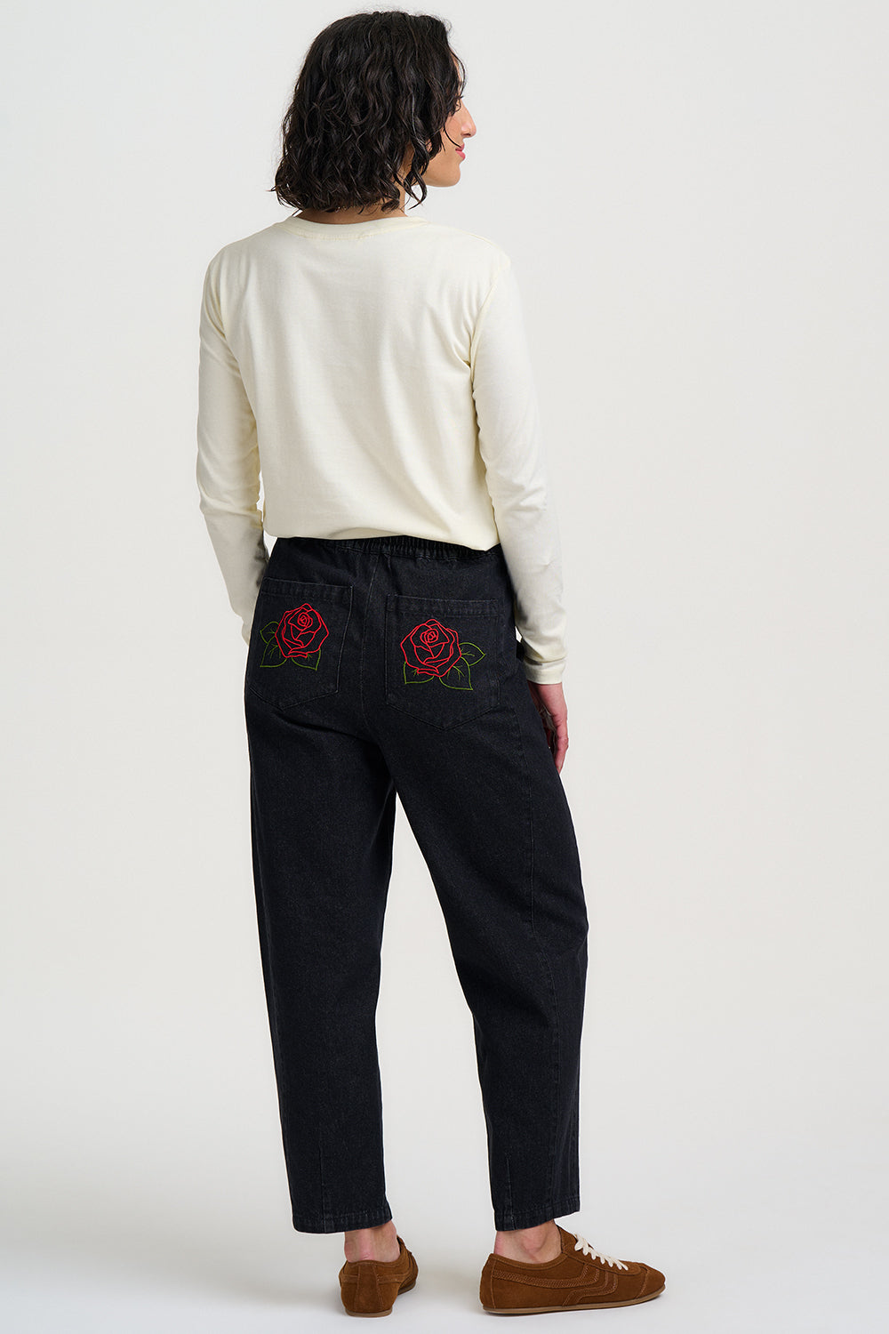 Person wearing black pants with red floral embroidery on a white background