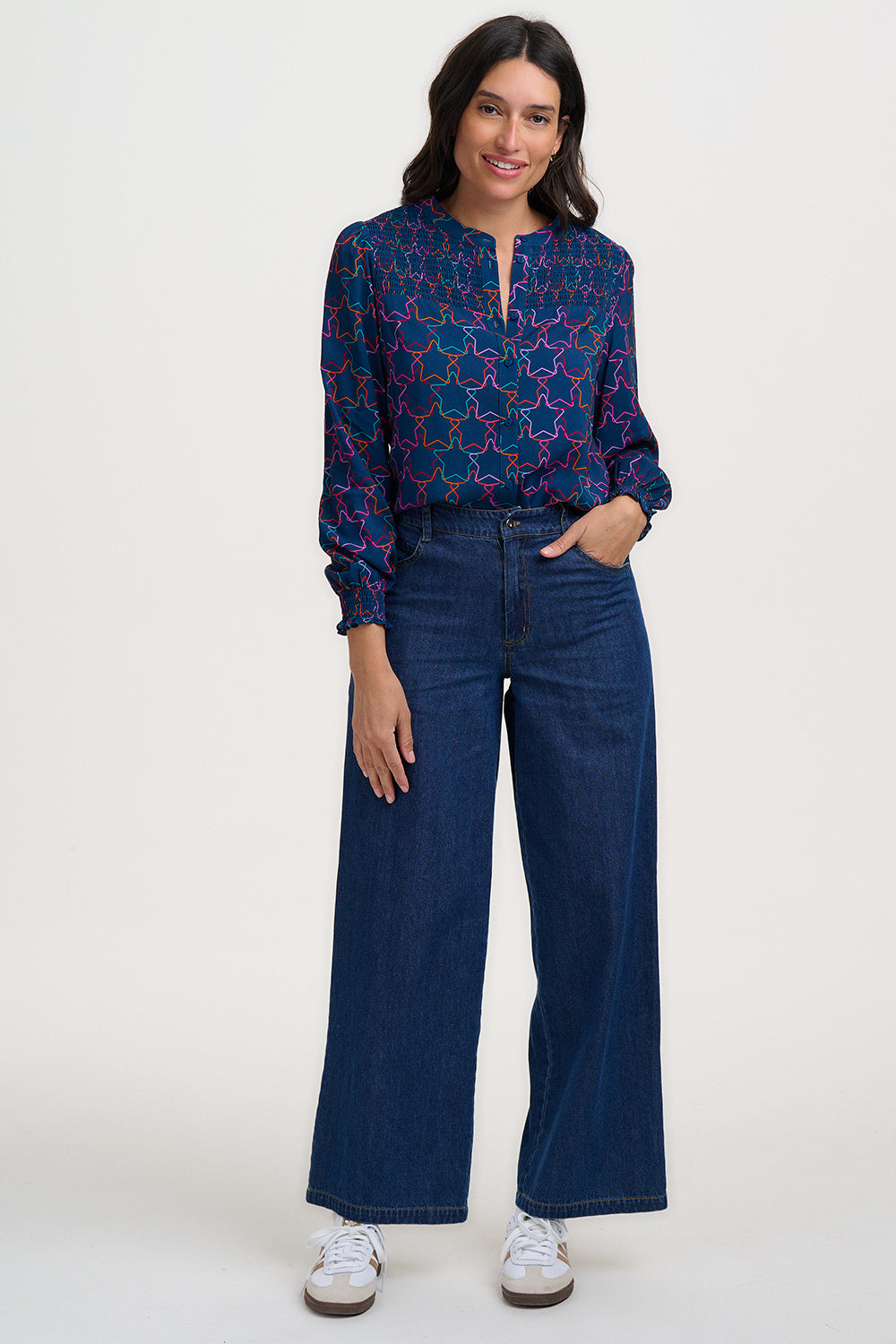 Woman wearing a blue patterned blouse and dark blue jeans on a white background