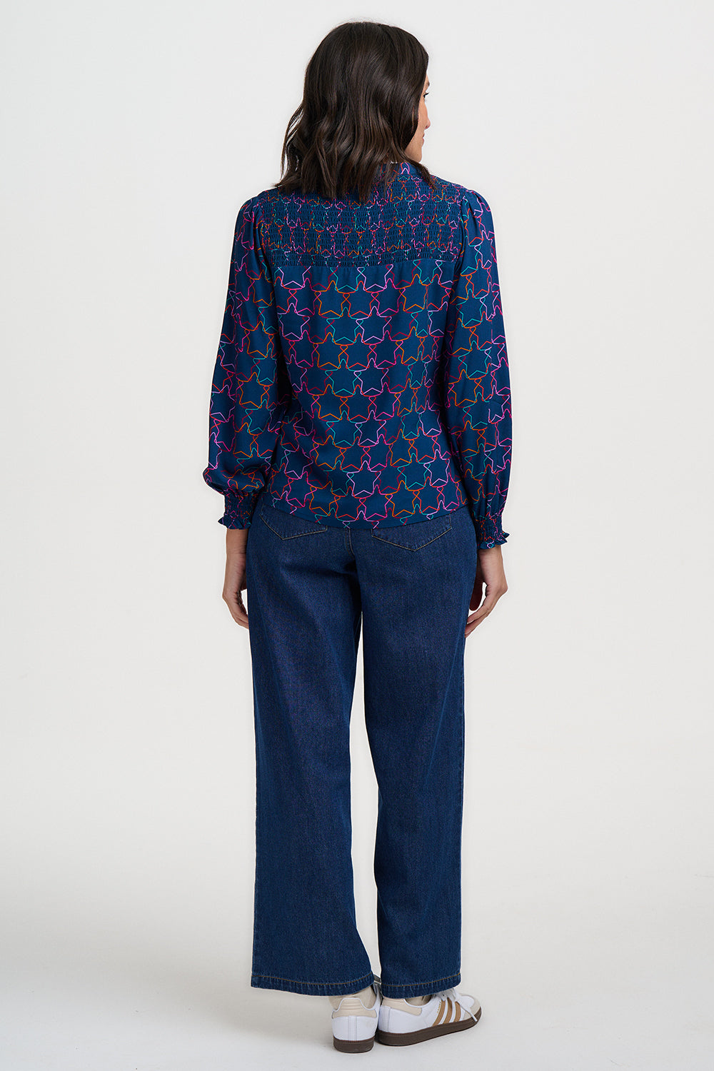 Woman wearing a blue patterned blouse and dark pants on a white background