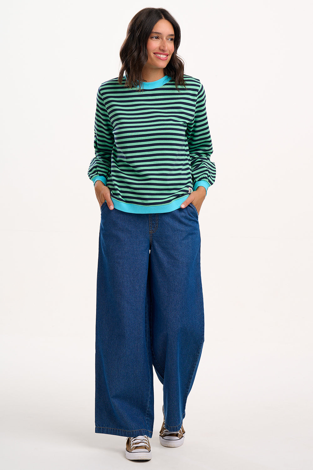 Sugarhill Brighton model wearing a green and black striped sweater with blue pants on a white background