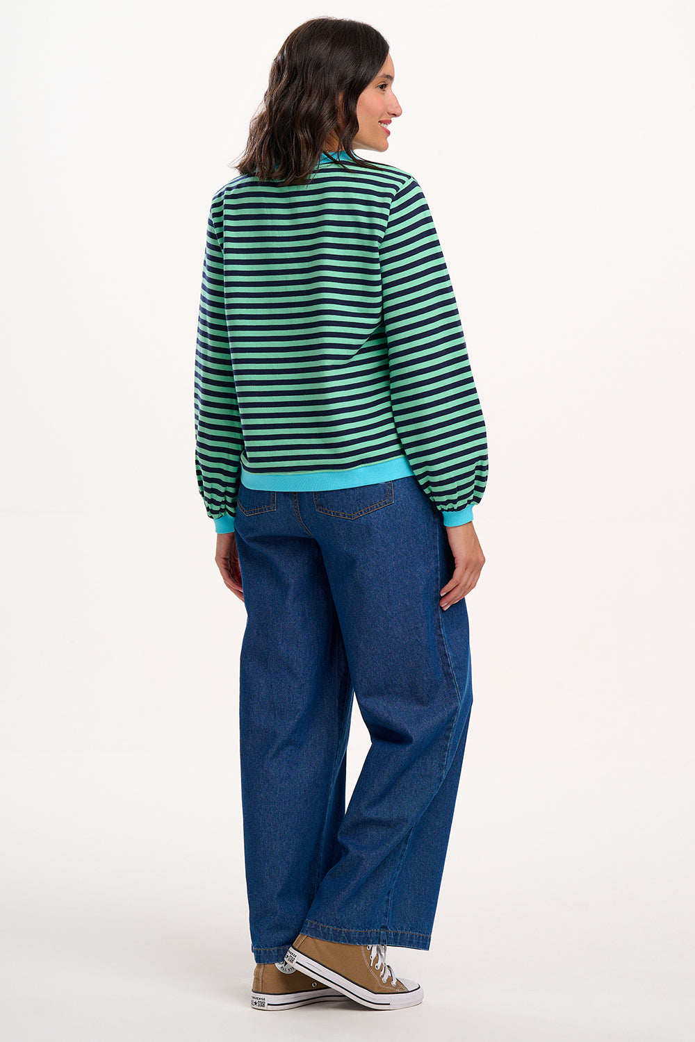 Sugarhill Brighton model wearing a green and black striped sweater with blue pants on a white background