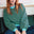 Sugarhill Brighton model wearing green and blue striped sweatshirt on a sofa. 