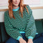 Sugarhill Brighton model wearing green and blue striped sweatshirt on a sofa. 