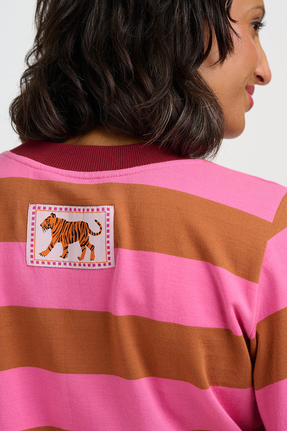 A close-up back view of a woman wearing a pink and brown horizontally striped sweatshirt with a tiger patch on the upper back.