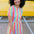 A woman smiling and wearing a multicolored tiered midi jersey dress with a round neckline and short puff sleeves.