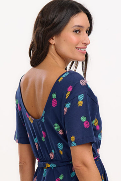 A navy midi jersey dress with a multicolor pineapple print, featuring a low scoop back, short sleeves, and an elasticated waistband with a tie belt. The dress is modeled by a woman standing against a white background.