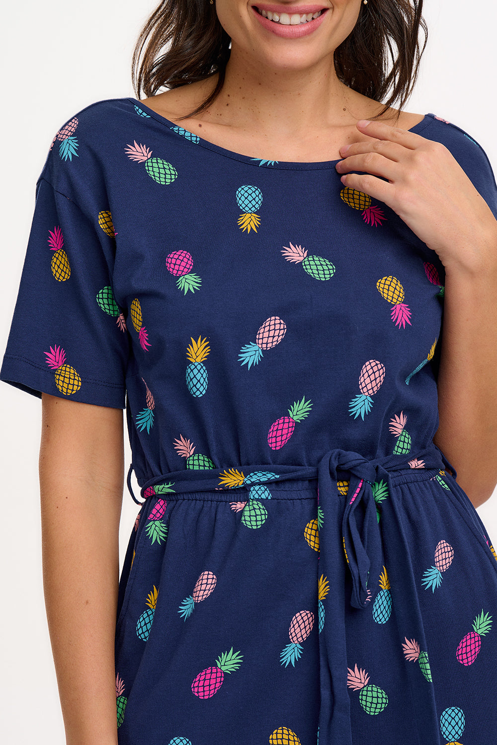 A navy midi jersey dress with a multicolor pineapple print, featuring a low scoop back, short sleeves, and an elasticated waistband with a tie belt. The dress is modeled by a woman standing against a white background.