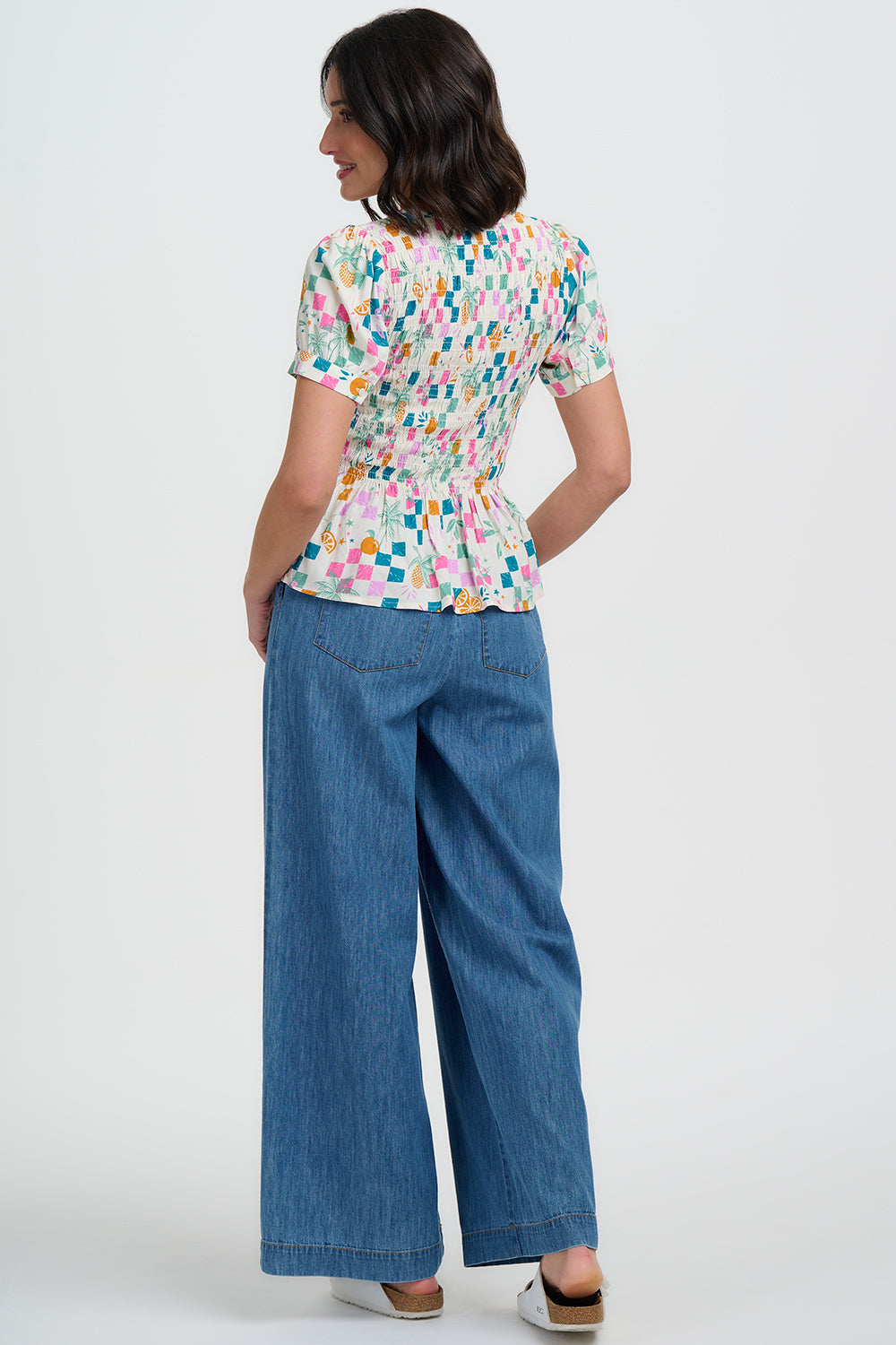 Woman wearing a colorful patterned top and blue jeans on a white background