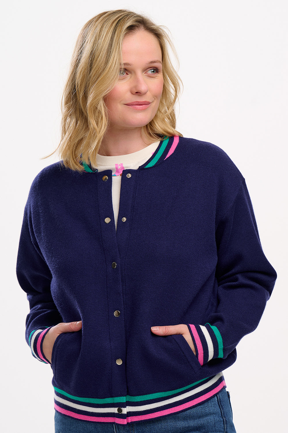 A navy blue knitted bomber jacket with sports stripes in pink, white, and green around the neck, hem, and sleeve cuffs. The jacket features a round neckline, long sleeves, and popper fastening.