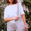 Woman wearing a white t-shirt and colorful striped pants holding a matching bag outdoors.