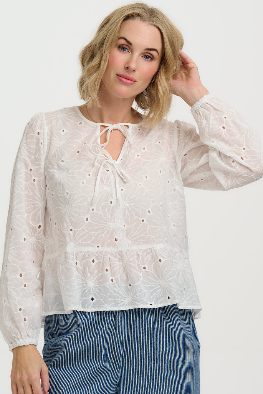 Woman wearing a white blouse with intricate details on a plain background