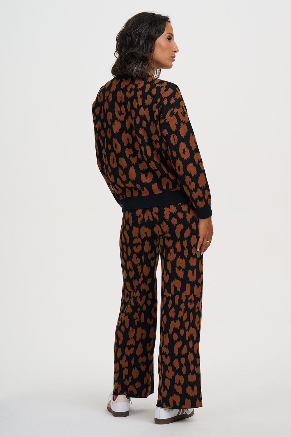 A woman shown from the back wearing a matching long-sleeve top and wide-leg trousers set in a brown and black leopard print, against a plain white studio background.