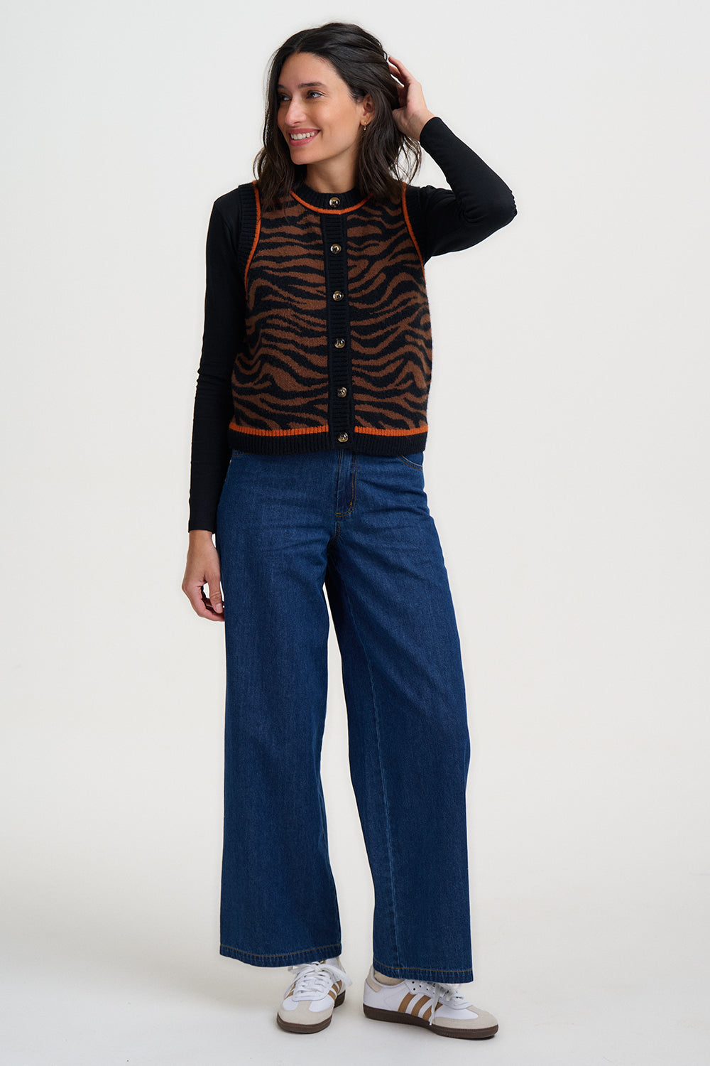Woman wearing a black cardigan with orange zebra pattern and blue jeans on a white background