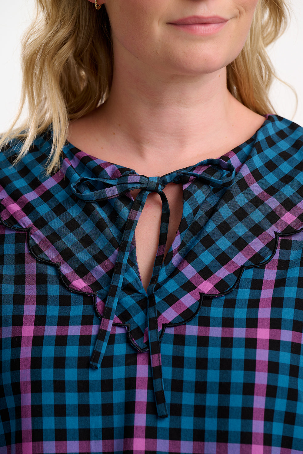 Close-up of Sugarhill Brighton model wearing a blue and pink plaid dress with a ruffled neckline.